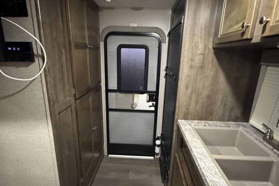 RV rental interior: A practical galley kitchen with double sink & fridge, storage cabinets, and an exit door, maximizing space.