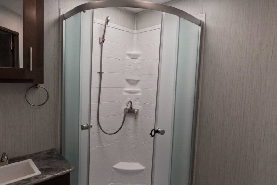 Compact RV rental bathroom featuring a corner shower, vanity with sink, and toilet. Ready for your adventure!