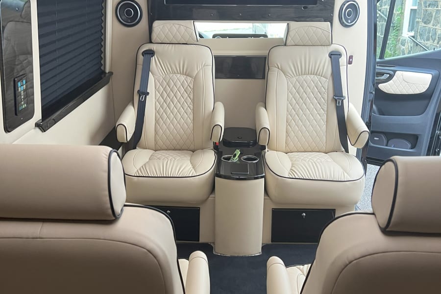 Step into luxury with this RV rental. A spacious interior boasts plush cream seats, a large TV, and custom amenities for comfort.