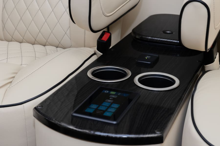 Luxury RV rental interior: cream quilted leather seating, central console with cup holders, USB charger, and touchscreen controls.