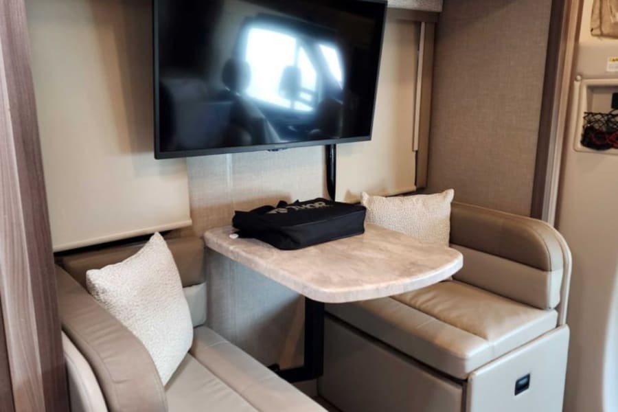 RV rental interior: A cozy dinette setup featuring comfortable bench seating, a table, and a wall-mounted TV for entertainment.