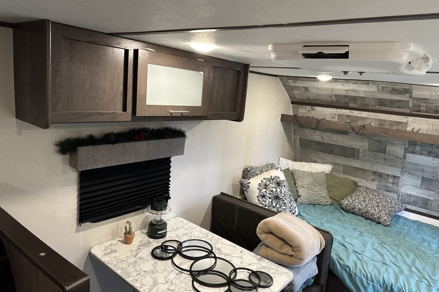 RV rental interior: cozy bedroom area with blue comforter, dining table, and dark wood overhead storage.
