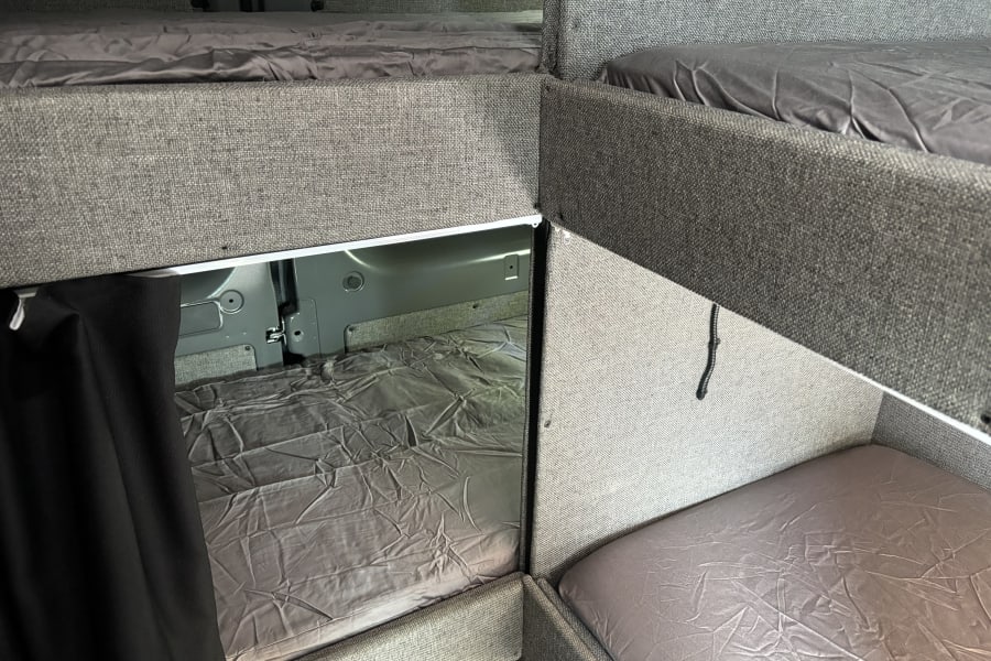 Inside an RV rental: multiple bunk beds with grey sheets, maximizing sleeping space in a compact camper van.