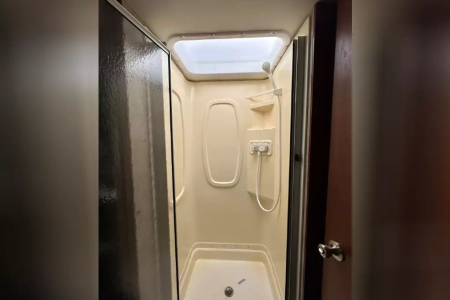 Bright, compact RV rental shower stall with an overhead skylight and handheld showerhead.