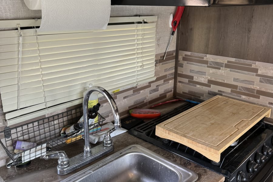 RV rental kitchen setup with sink, stovetop, microwave, and paper towel holder over window.
