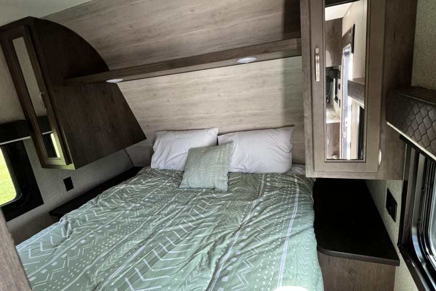 Cozy RV rental bedroom with a comfy bed, overhead storage, and a window. Perfect for your travel adventures!
