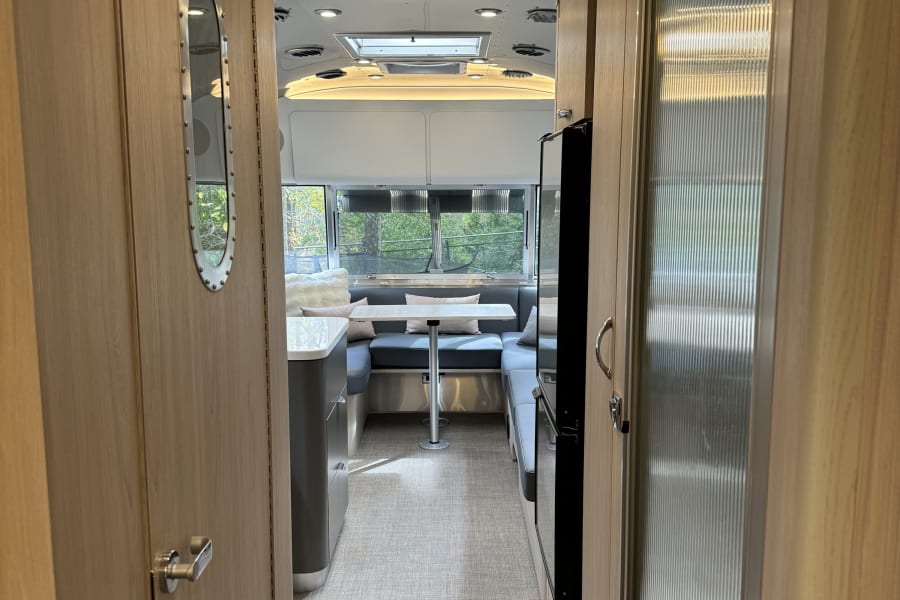 Inside a sleek RV rental: light wood, shiny ceiling, and a bright dinette with large windows. Ready for adventure!