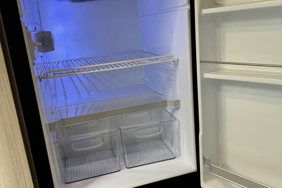 Clean, empty RV rental refrigerator interior with blue light, ready for road trip food. Compact fridge for camping adventures.