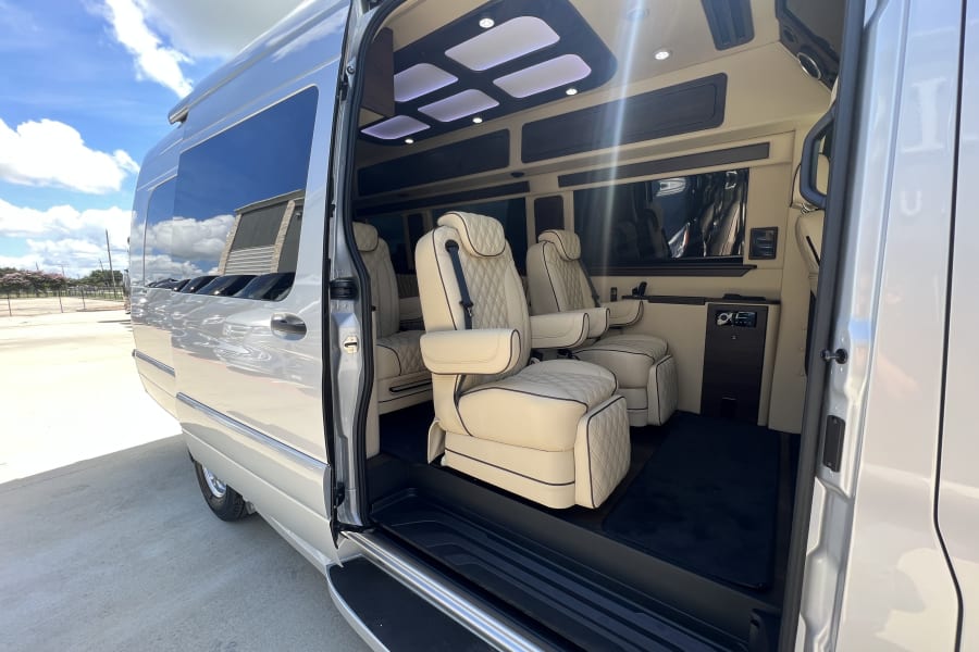 Experience a luxury RV rental. This spacious van's interior features cream, quilted seats, ambient lighting, and dark wood accents.