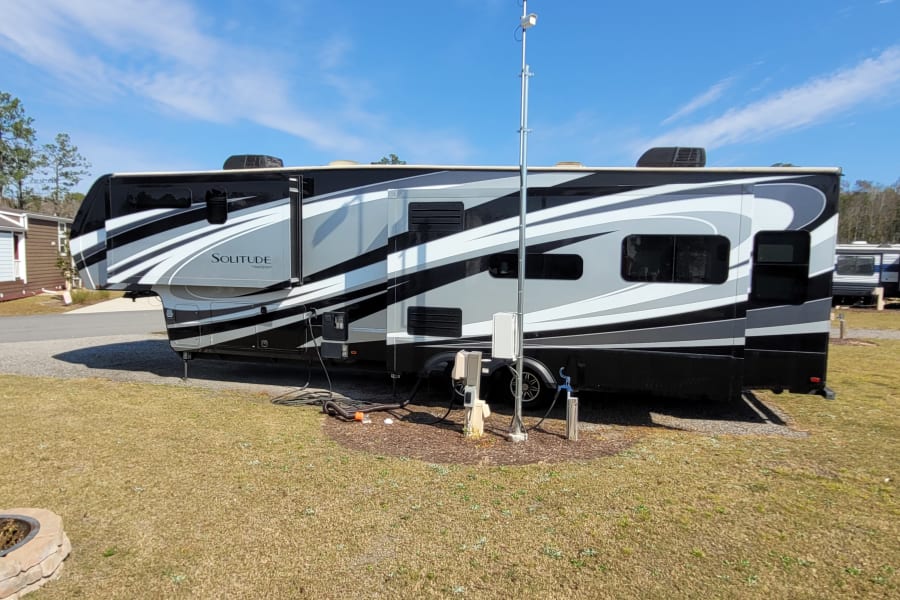 A large, modern "Solitude" fifth-wheel RV at a sunny campsite with hookups, perfect for your RV rental getaway.