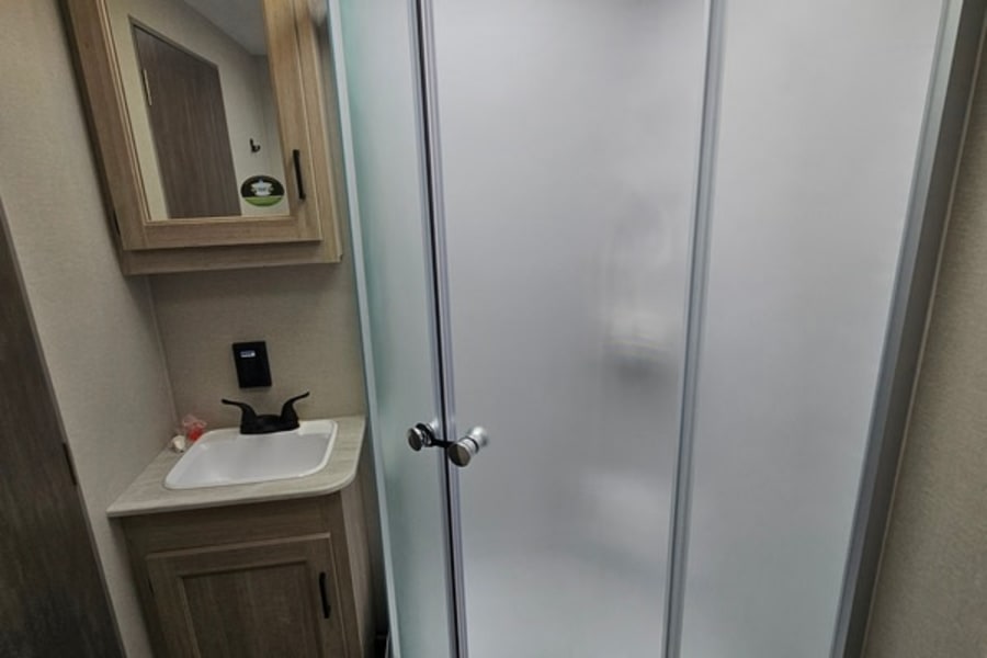This RV rental features a compact, modern bathroom with a corner shower (frosted glass), sink, and mirrored medicine cabinet.