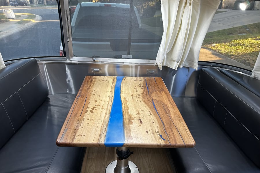 Stylish rv rental interior features a custom wood & blue resin table, sleek black seating, and bright windows.