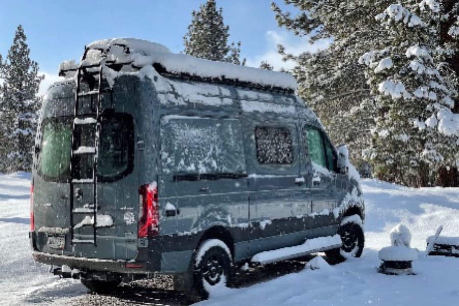 Snow-covered gray RV rental van in a serene winter landscape. Perfect for your next cold-weather adventure.