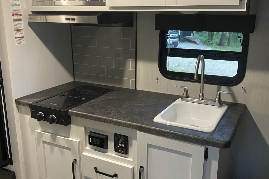 RV rental kitchen: Features a Greystone microwave, 2-burner cooktop, sink, and modern white cabinets with dark hardware.
