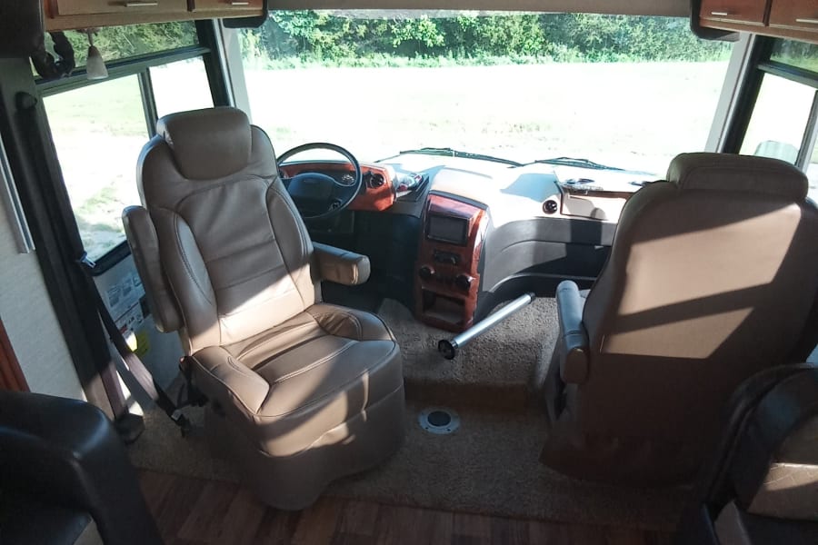 Spacious RV rental cabin interior featuring plush driver and passenger seats, detailed dashboard, and large front window.
