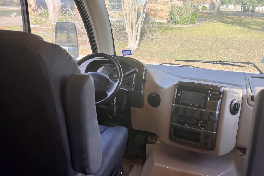 Step inside an RV rental: detailed view of the driver's seat, steering wheel, and modern dashboard with outside scenery.