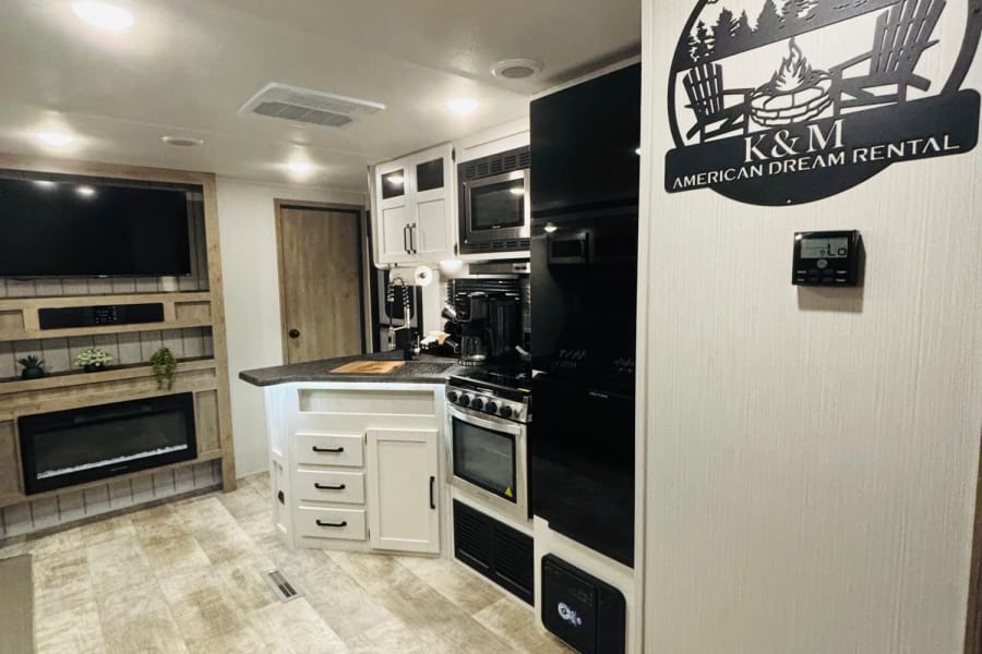 Modern RV rental interior with a fully equipped kitchen, living area featuring a TV and fireplace, and custom K&M sign.