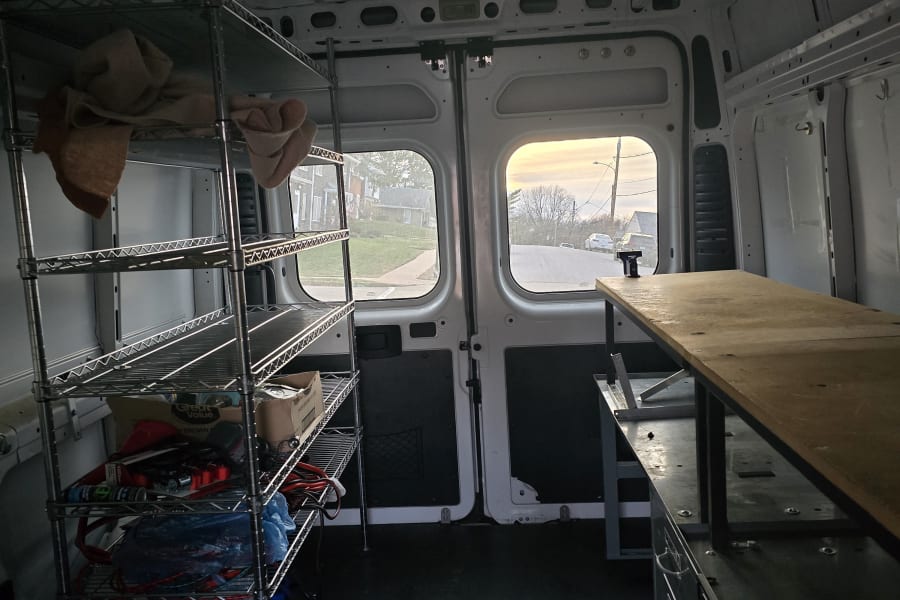 Cargo van interior optimized for RV rental or mobile work, featuring practical metal shelving and a sturdy workbench.