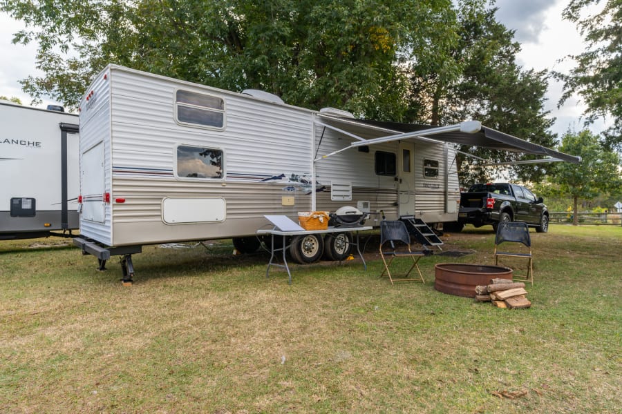 This RV rental is set up for a relaxing day at the campsite, complete with an extended awning, grill, and fire pit.