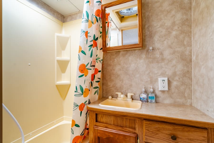 Inside this functional RV rental: a compact bathroom with a yellow shower, a vibrant orange shower curtain, and a wooden vanity.