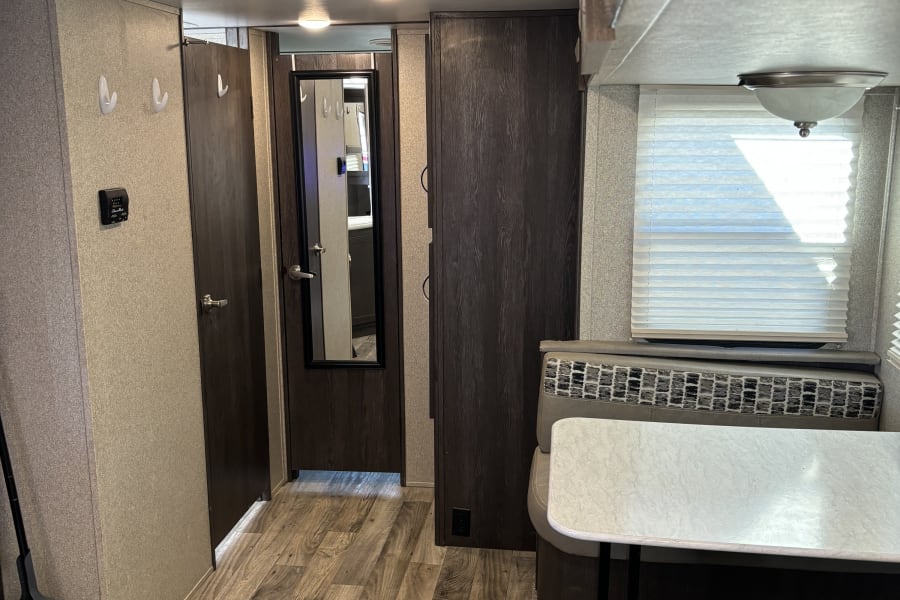 Compact RV rental interior featuring a dinette, wood-look flooring, and hallway with dark wood doors. Functional living space.