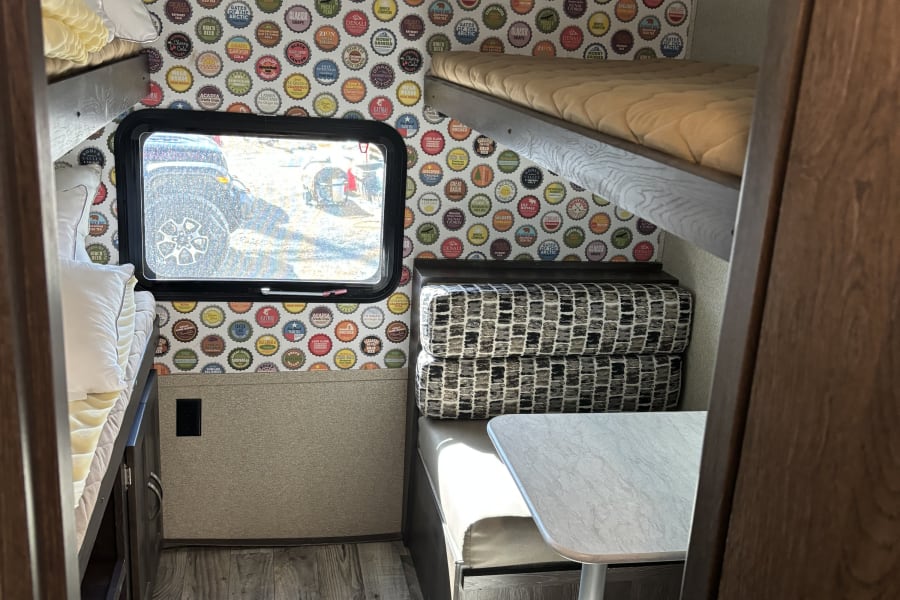 Cozy rv rental interior with unique national park bottle cap wallpaper, bunk beds, and a dinette. Perfect for travel adventures!
