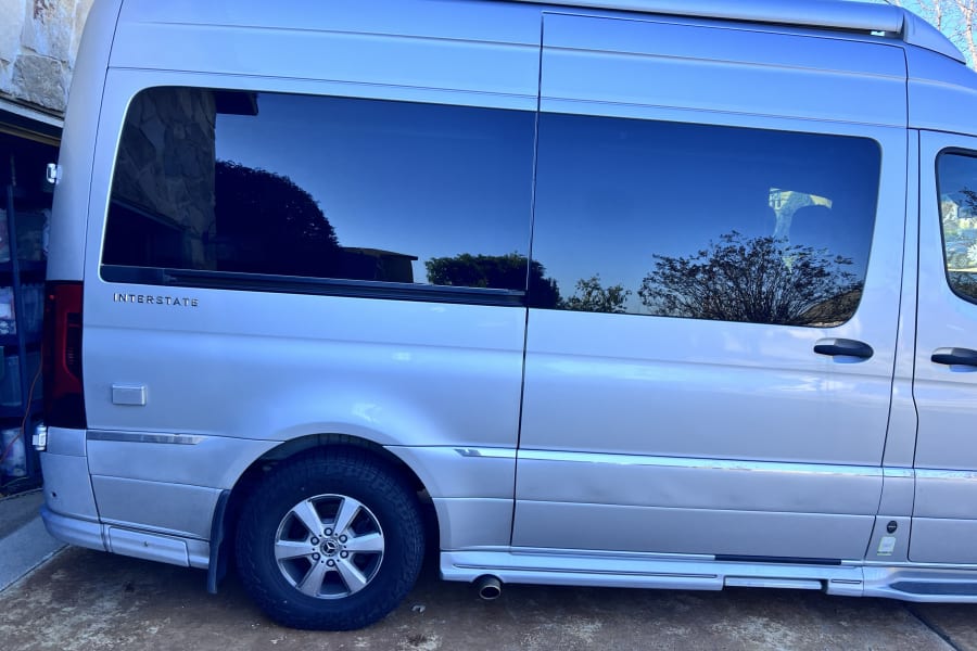 Silver Airstream Interstate RV rental van parked outdoors, showing tinted windows and side running boards.