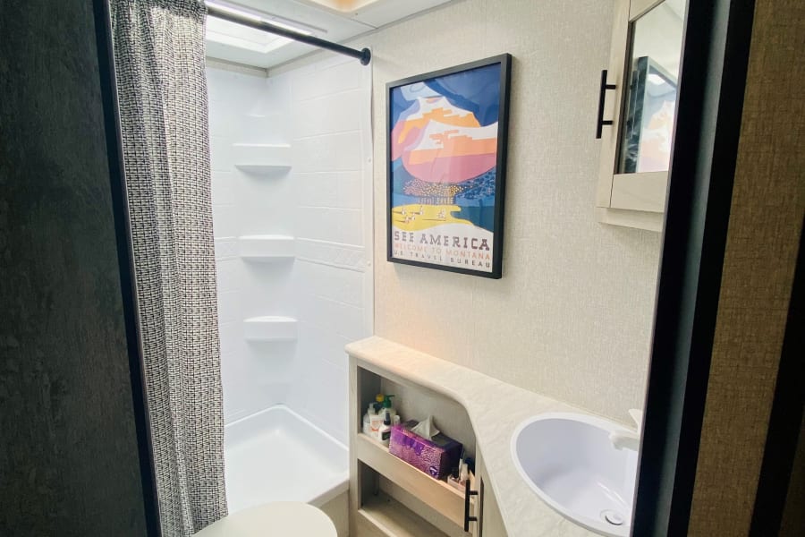 Inside a clean, compact rv rental bathroom, featuring a shower, toilet, vanity with sink, and wood-look flooring.