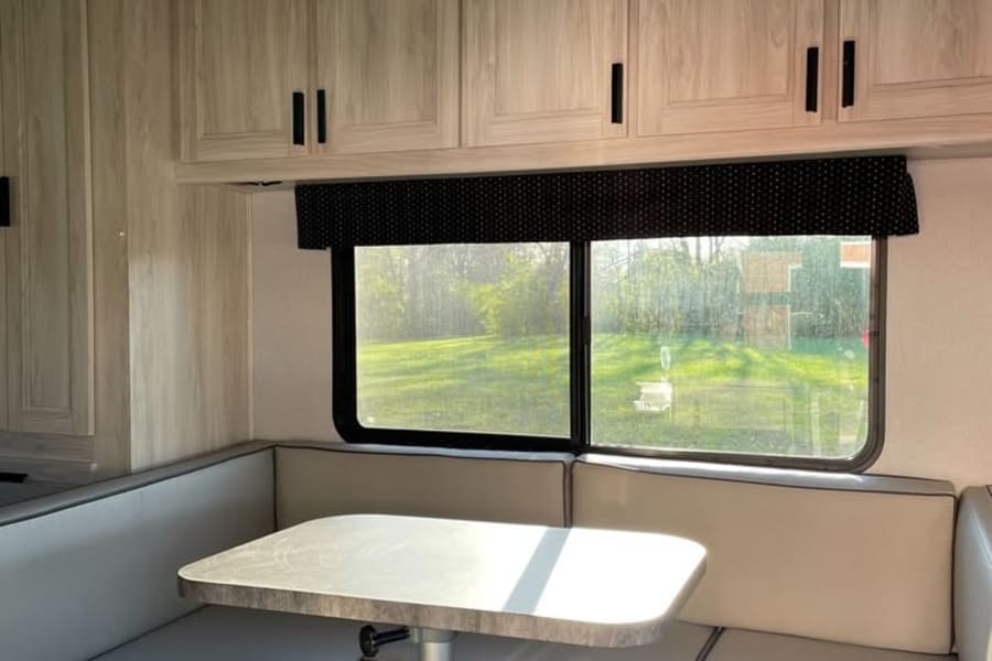 Cozy RV rental dinette featuring U-shaped seating, table, overhead cabinets, and a scenic window view.