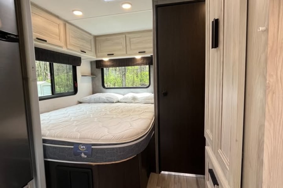 Step inside this inviting rv rental bedroom, featuring a comfortable bed, modern storage, windows with green views, and a skylight.