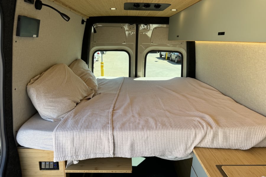 RV rental: Modern camper van bedroom featuring a large bed, bamboo ceiling, and custom-integrated controls.