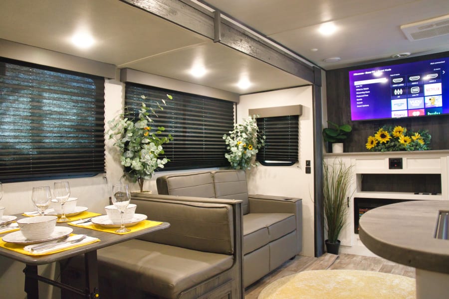 This modern RV rental features a comfortable living and dining area with a smart TV and decorative plants.