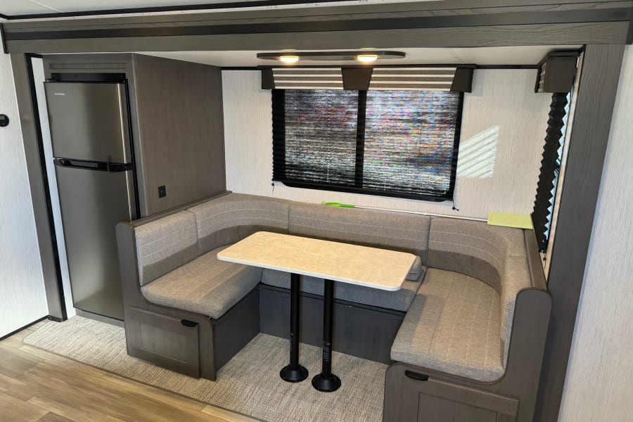 Inside an RV rental: a U-shaped dinette with a table, large window, and built-in refrigerator.