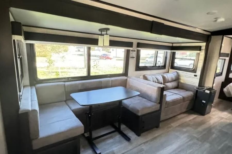 Spacious RV rental interior featuring a U-shaped dinette, comfortable sofa, and bright windows in the living area.