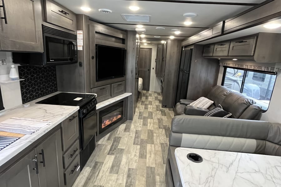 RV rental: Modern interior with kitchen, recliners, and electric fireplace in the spacious living area.
