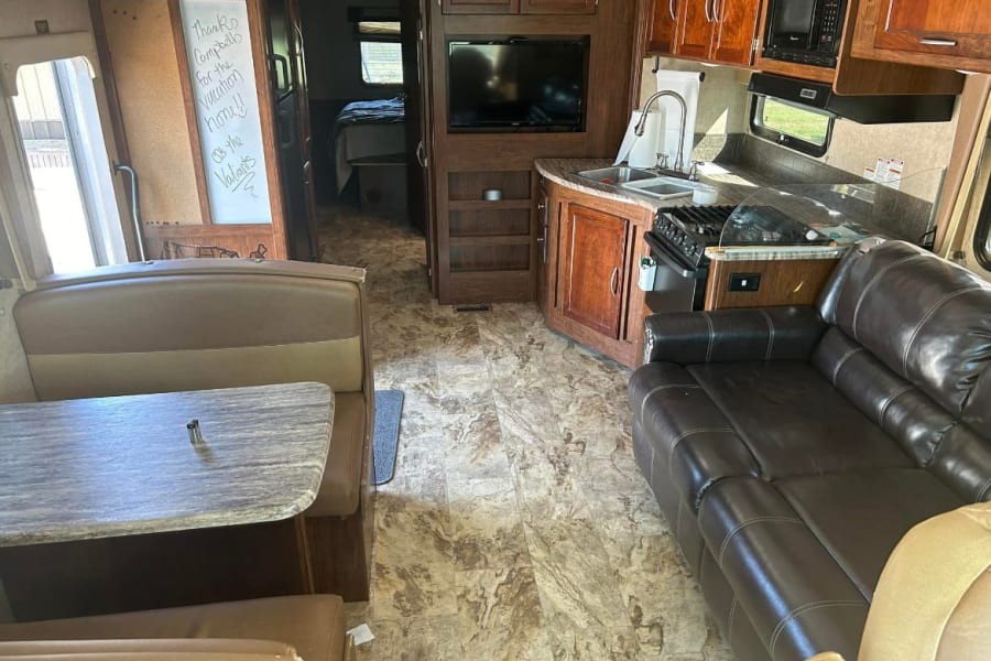 RV rental interior showing a kitchen, dinette, living area with couch, and a peek into the bedroom. Perfect for your next trip.