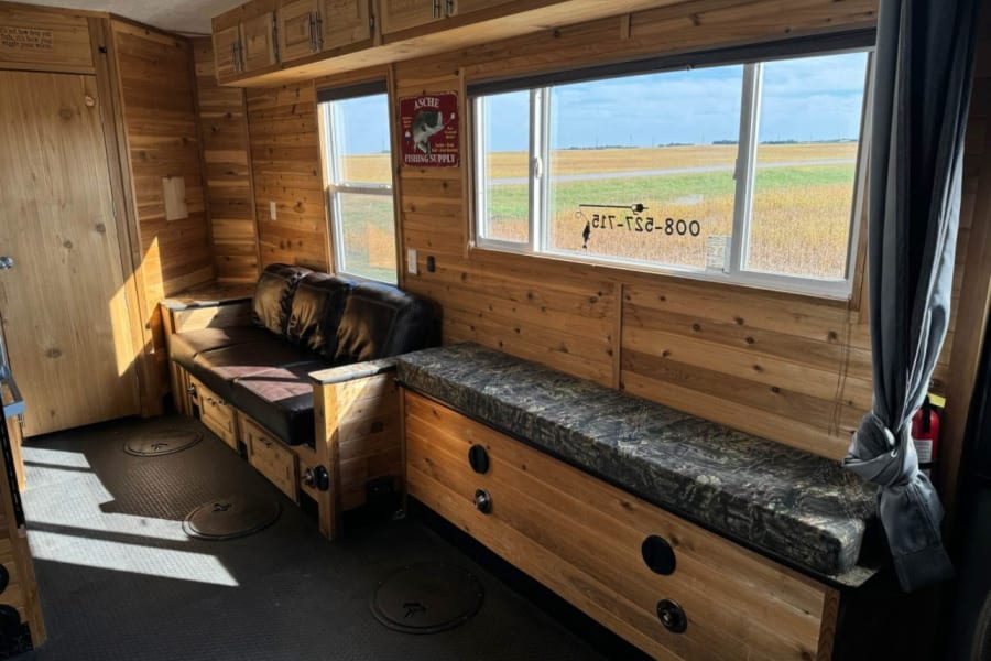 Cozy wood-paneled ice fishing house interior for rv rental, featuring seating, cabinets, and floor fishing access.