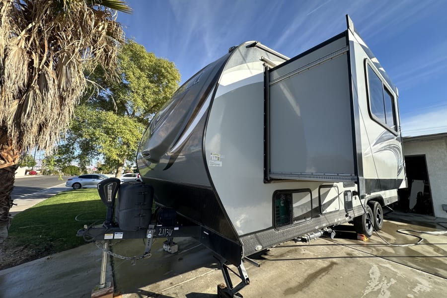 Spacious grey travel trailer, ready for your next adventure. Perfect RV rental for road trips. Parked outdoors with palm trees.