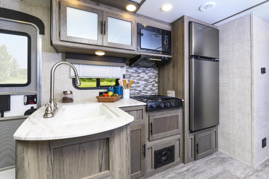 Modern RV rental kitchen featuring a sink, stovetop, microwave, and refrigerator, ideal for your next adventure.
