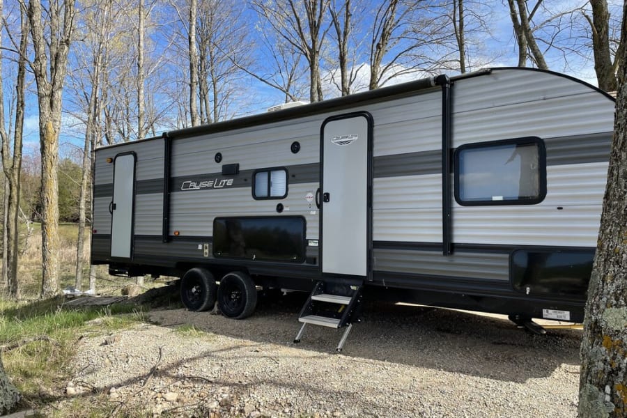 This large grey RV rental is nestled among trees on a gravel pad, ideal for camping trips.