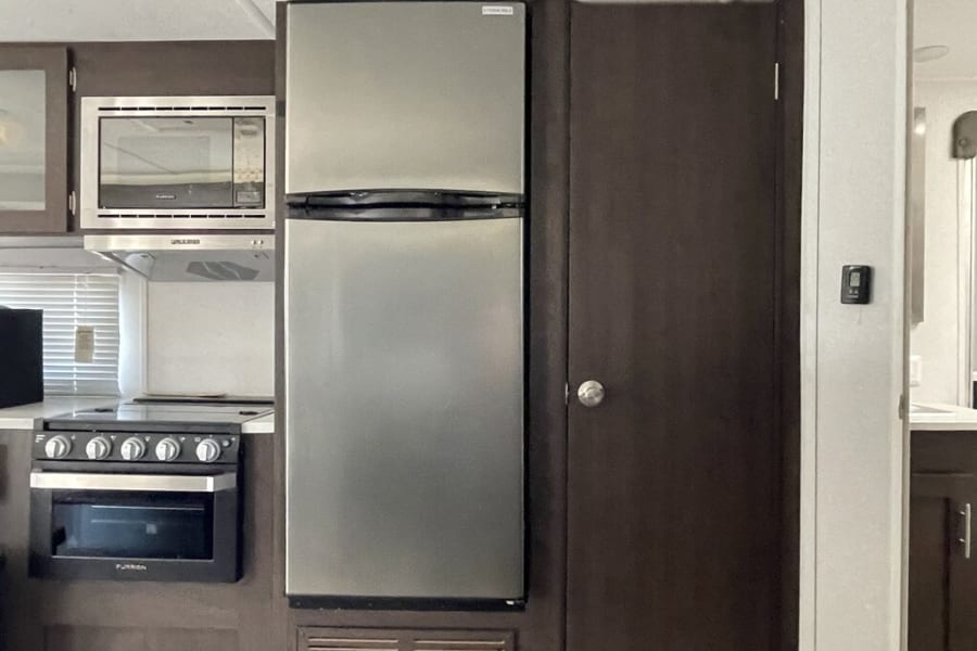 RV rental kitchen: This compact space features a tall stainless steel refrigerator, microwave, and black stove/oven. Dark wood cabinets.