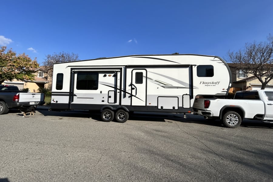 A large Flagstaff travel trailer RV rental, hitched to a white pickup truck, on a residential street with a dog.