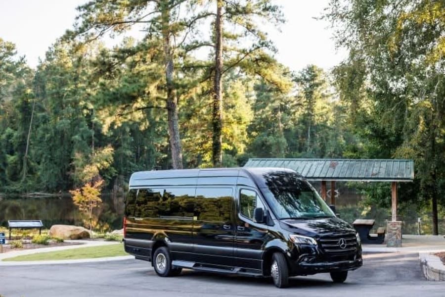 Sleek black Mercedes Sprinter van for rv rental, parked by a tranquil lake in a wooded park setting.
