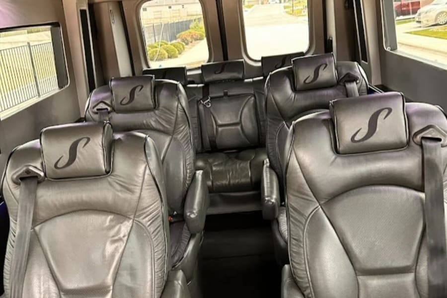 Spacious, luxurious van interior perfect for an rv rental. Features dark gray leather seats, overhead screens & blue ambient lighting.