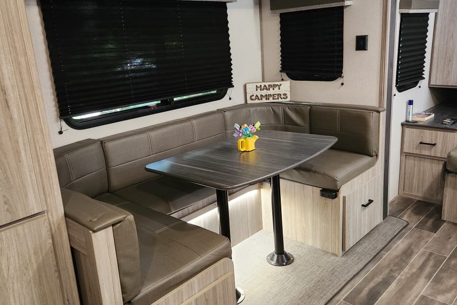 RV rental dinette area: U-shaped seating, dark table, black window blinds, and light wood cabinetry.