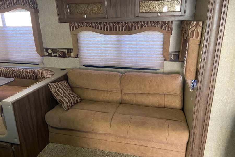 Comfortable RV rental interior featuring a dinette, sofa, and overhead cabinets. Perfect for your next road trip adventure.