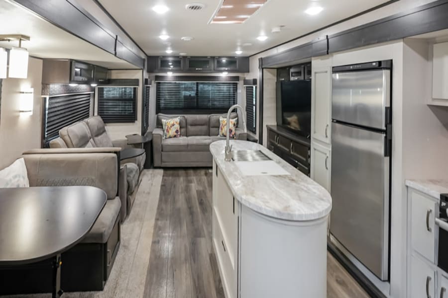 Spacious, modern RV rental interior features a living area, kitchen island, refrigerator, and dining nook.