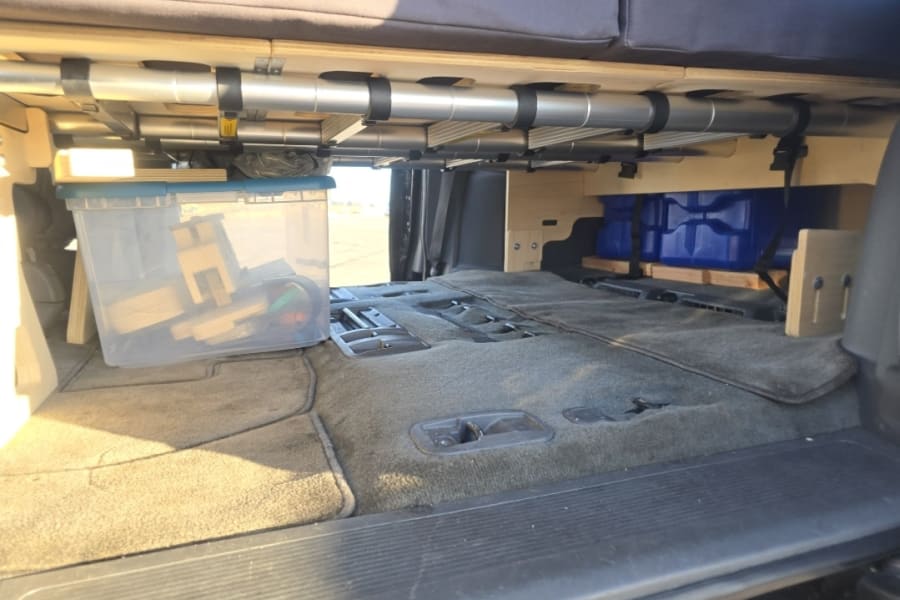 Inside an RV rental, a custom camper van setup with a raised bed platform and smart under-bed storage for gear.