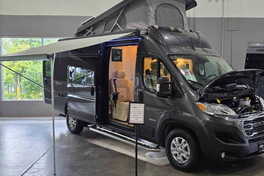 Dark gray Jayco camper van with pop-top and awning extended, interior illuminated and hood open, perfect for rv rental.