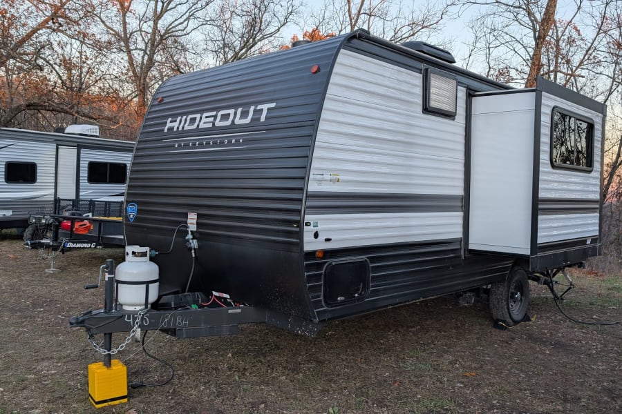 Black and white Hideout by Keystone RV, ready for an RV rental adventure. Features include an expanded pop-out and propane tank.
